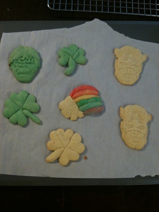 To make these shamrock sugar cookies, I took regular sugar cookie dough and dyed it green with regular food coloring, rolled it flat, and cut small hearts. Arrange three or four hearts point-side in to create either shamrocks or four-leaf clovers. Roll a small amount of green or regular cookie dough to finish with a stem. To make the rainbow, I reserved a small amount of sugar cookie dough to create the colored bands, dyeing each band with regular food coloring. I finished with a "cloud" of plain dough at one end. You could also make a pot-o-gold instead of the cloud.