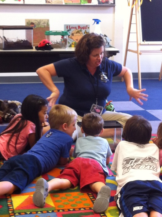 Ms. Dana demonstrating how the roaches "hiss" and move while the kids watch them in their terrarium.